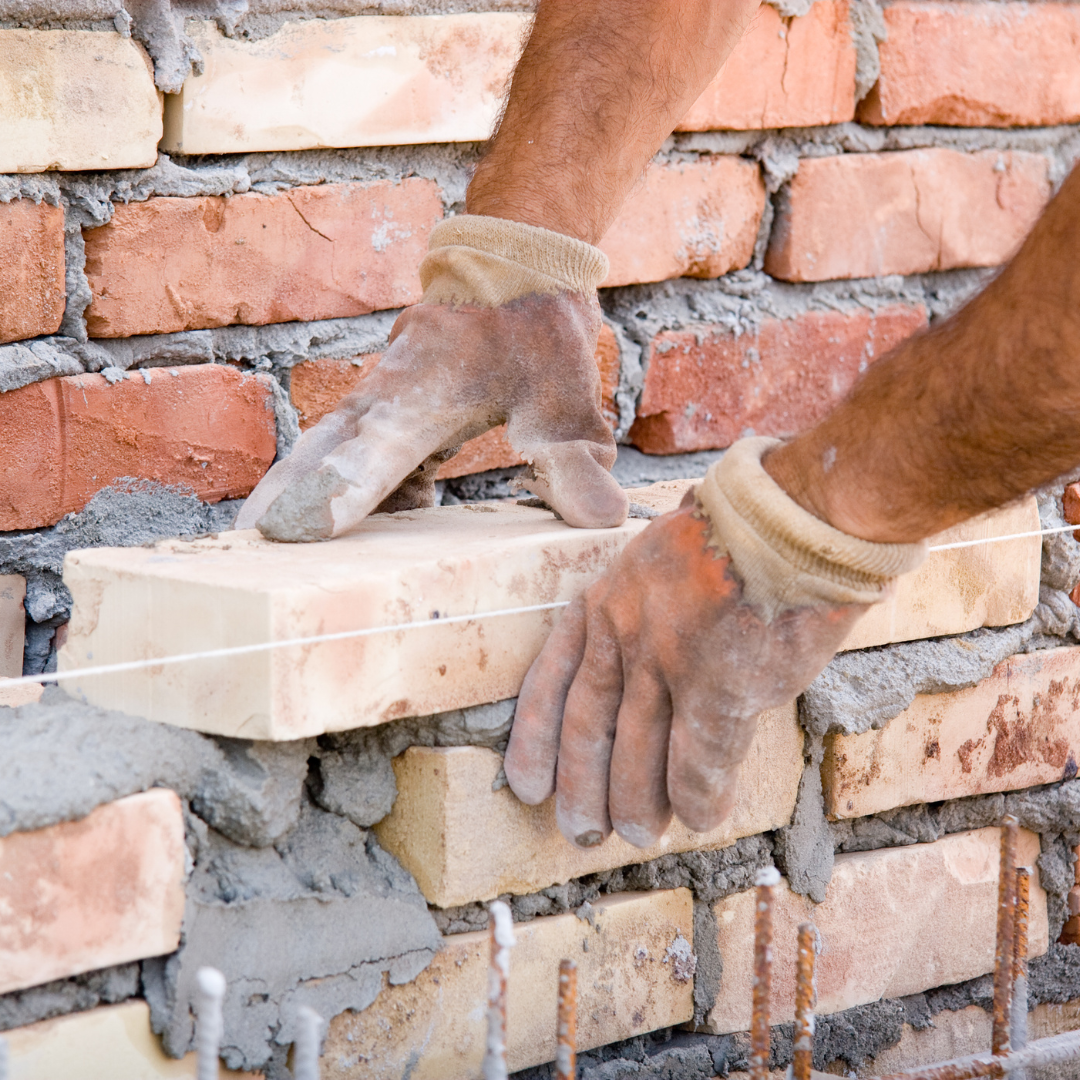 Masonry workers laying brick on a large building facade, representing professional commercial masonry contractors.